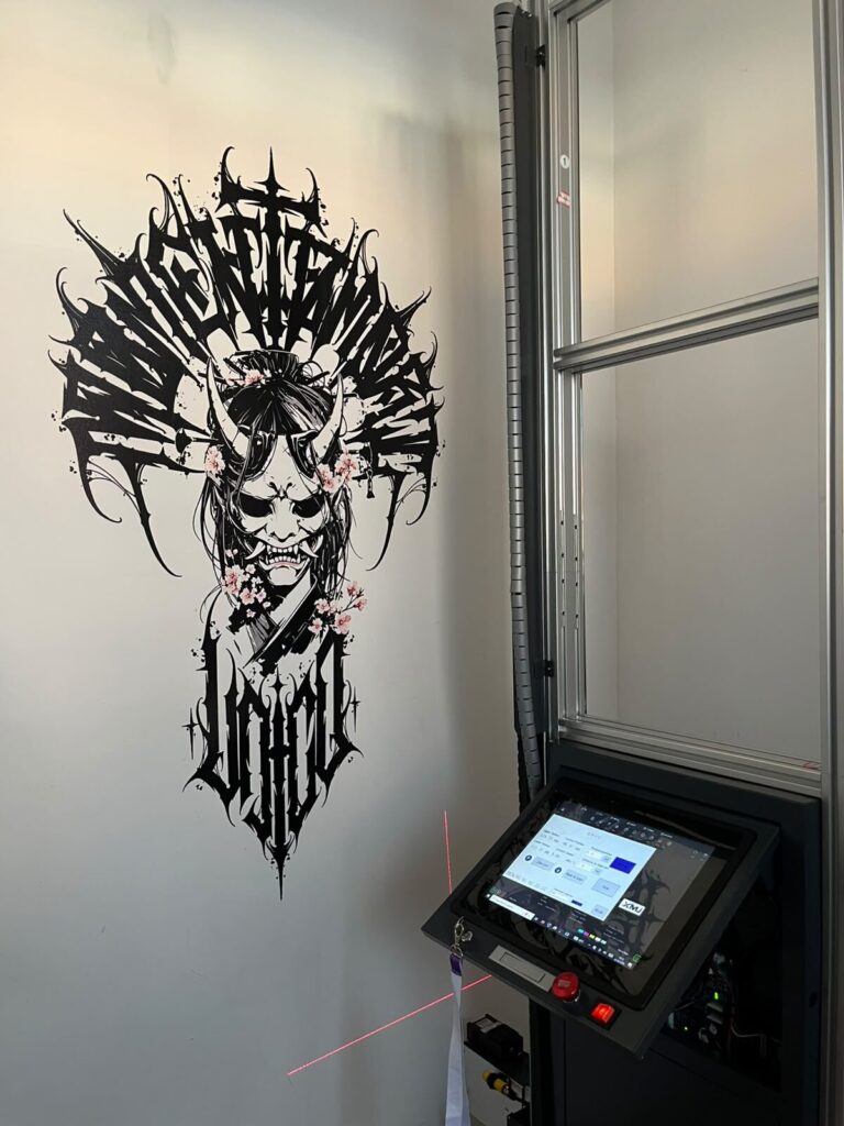 Vertical wall printer producing a sharp black and white Japanese demon mask illustration with floral accents.